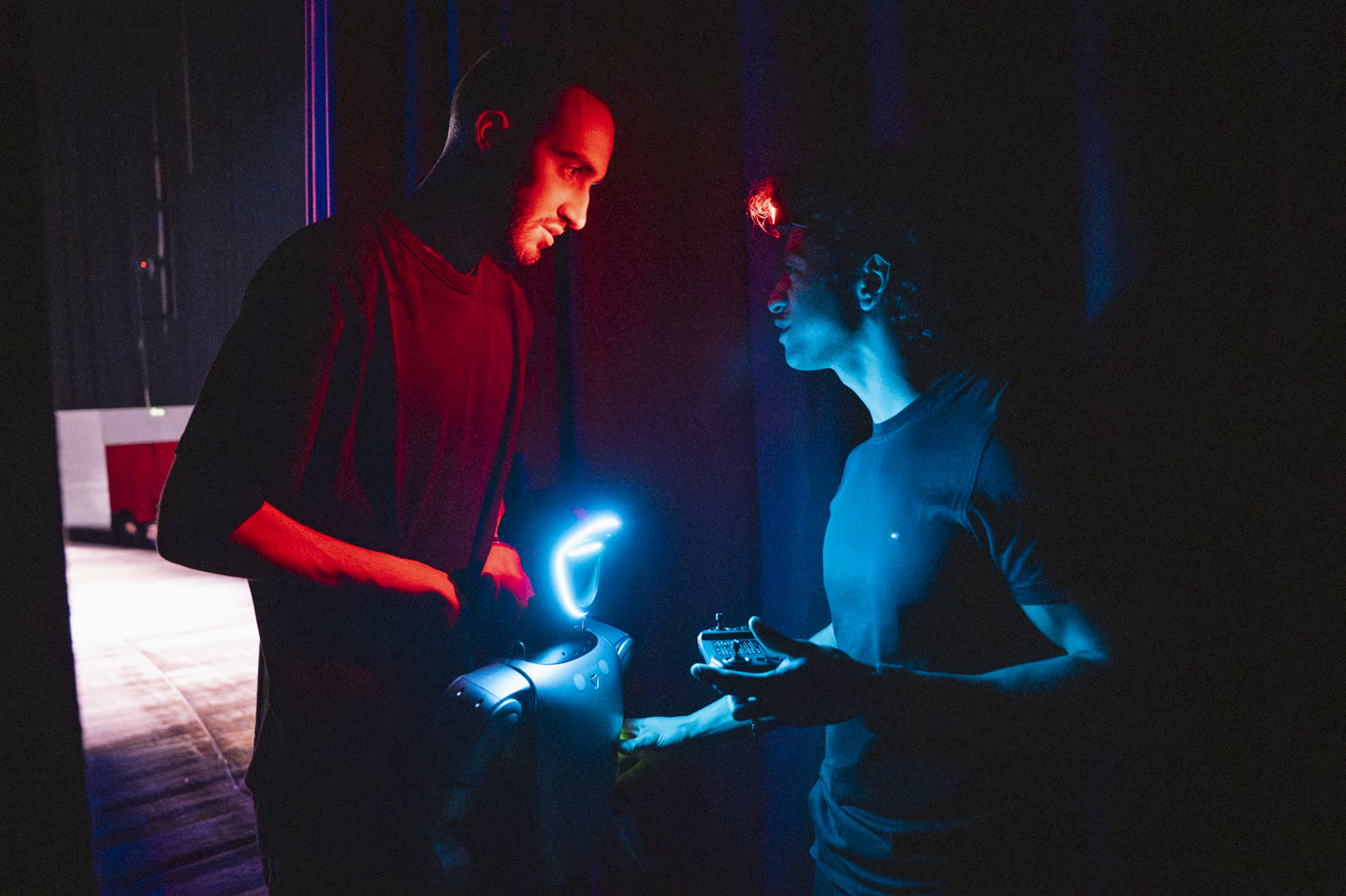 Backstage teatrale: due tecnici preparano un piccolo robot illuminato di neon
